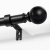Joydeco matte black adjustable curtain rod, 1-inch diameter, with spherical finial, mounted on a white wall.