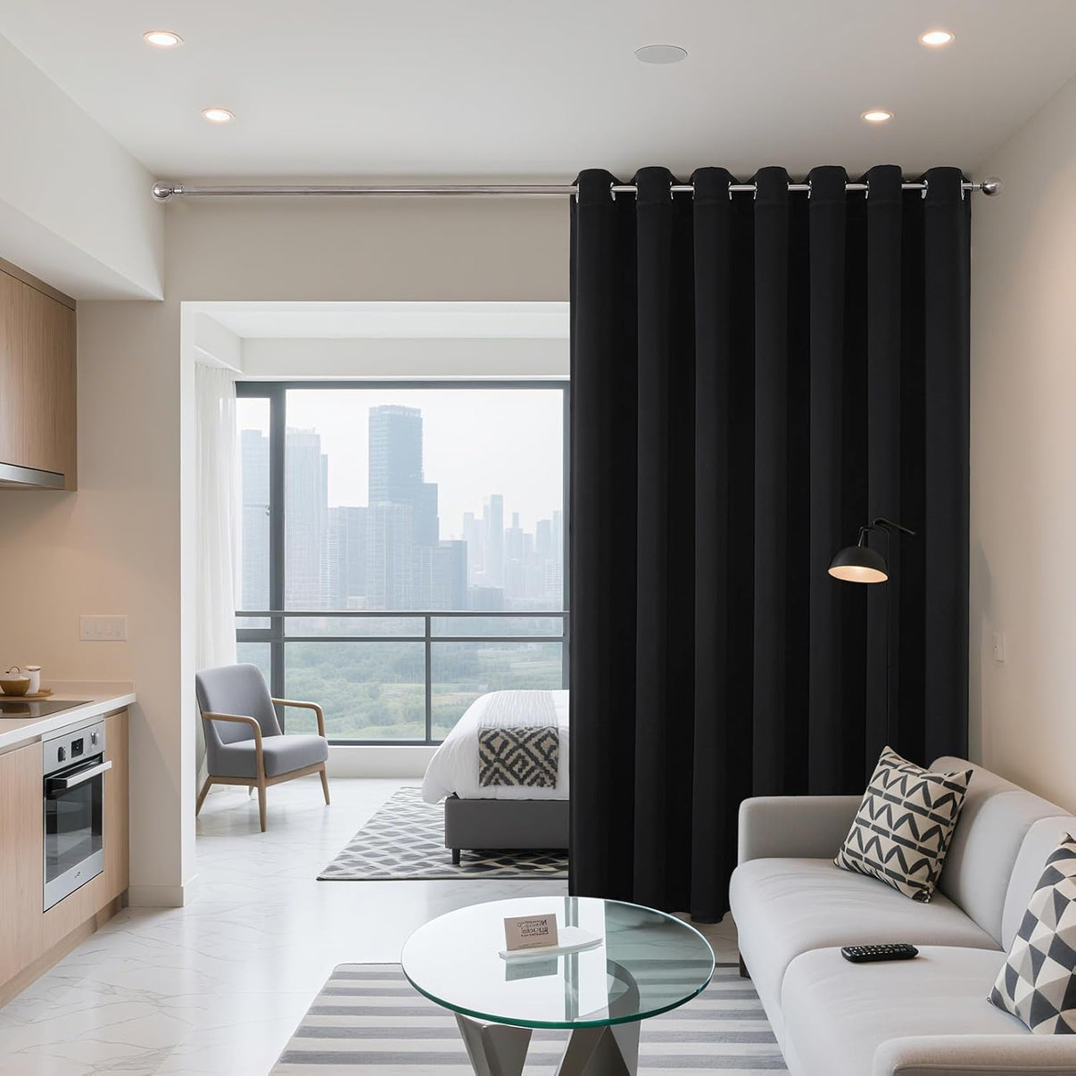 Extra wide black blackout grommet curtains dividing a studio apartment living area from bedroom, providing privacy.