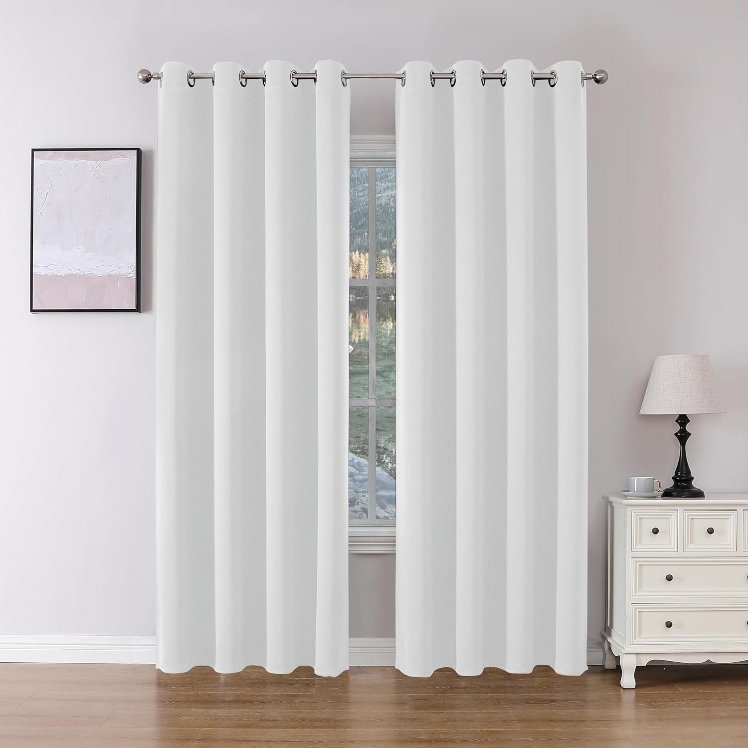 Two white Joydeco floor-length blackout curtains with grommet tops hang on a silver rod in a room setting.