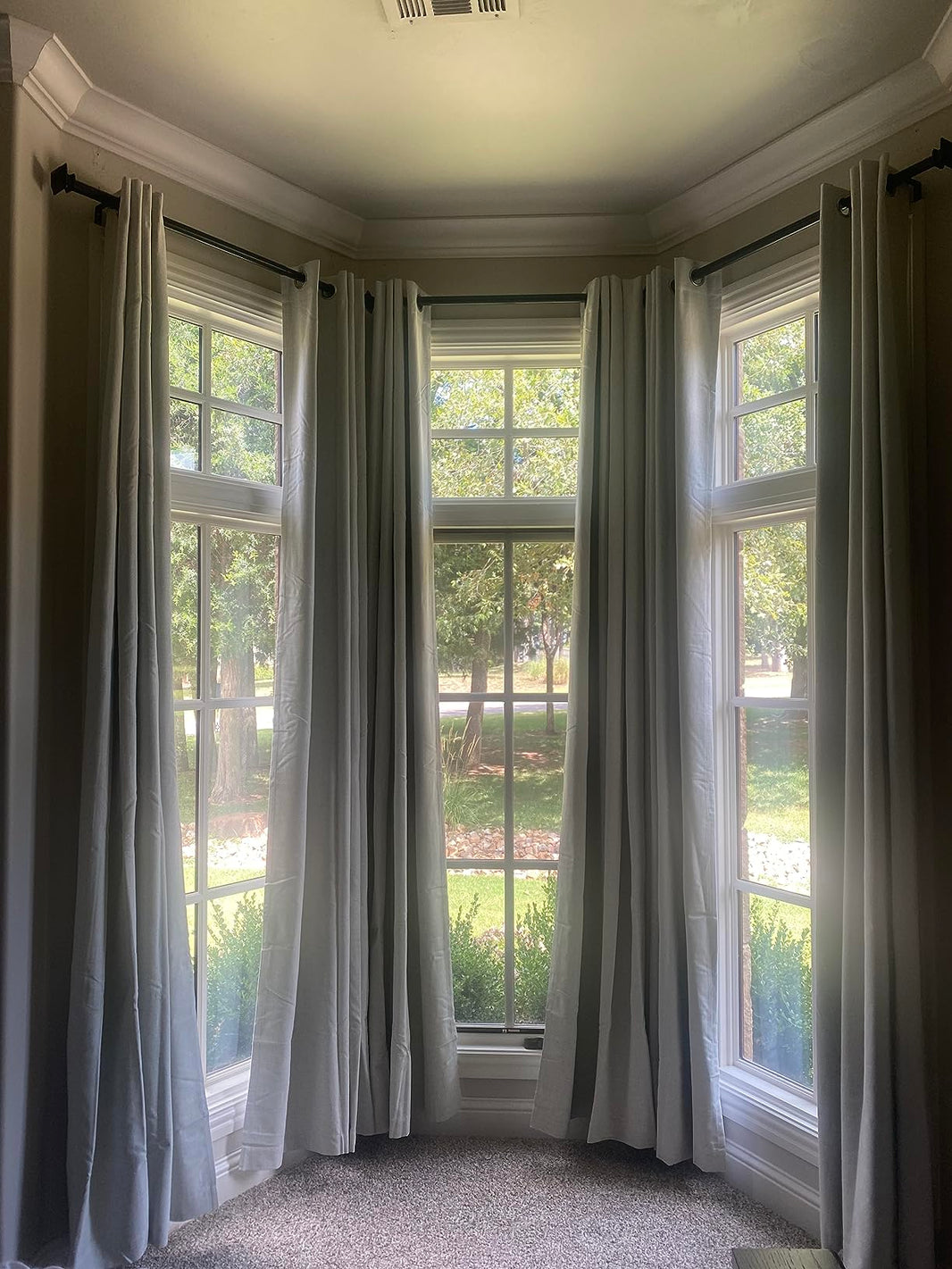 Light gray Joydeco blackout curtains hanging on dark rods in a bay window, showing drape and room setting.