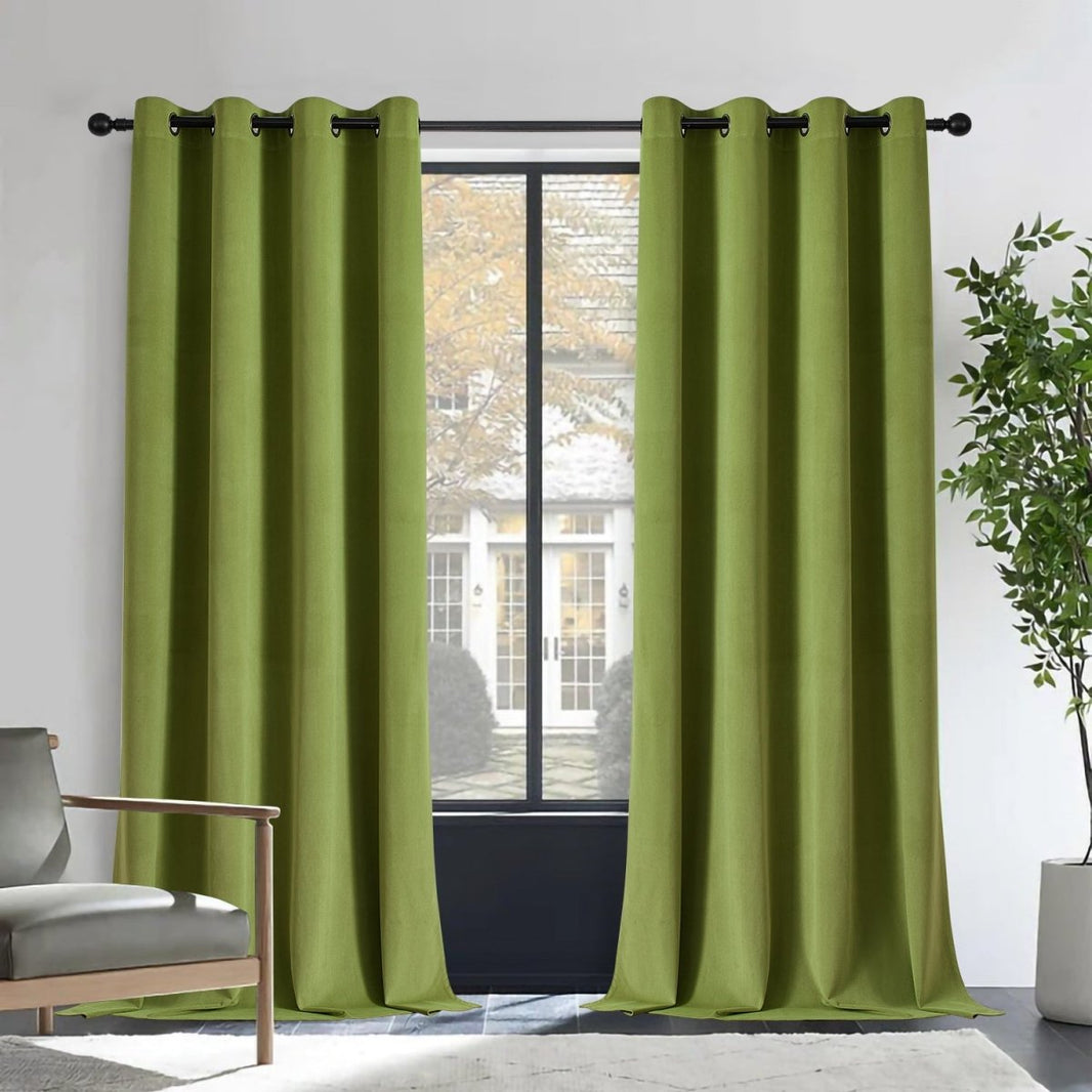 Joydeco moss green velvet blackout curtains, 2 panels with grommets, in a room with armchair and plant.