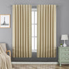 Two beige Joydeco 100% blackout curtains with rod pocket and back tab hang over a window in a bedroom.