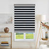 Joydeco motorized black and white striped dual shade with grey valance on window, hand holding remote for operation.