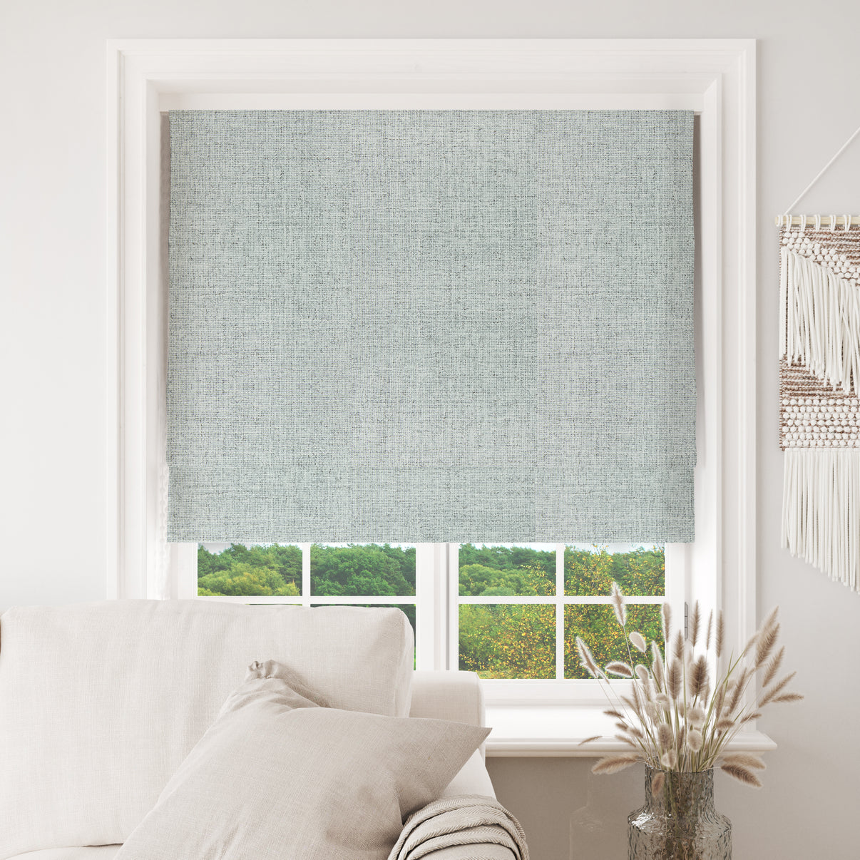 Celadon Joydeco blackout Roman shade, textured weave, installed on white window frame, view of trees.