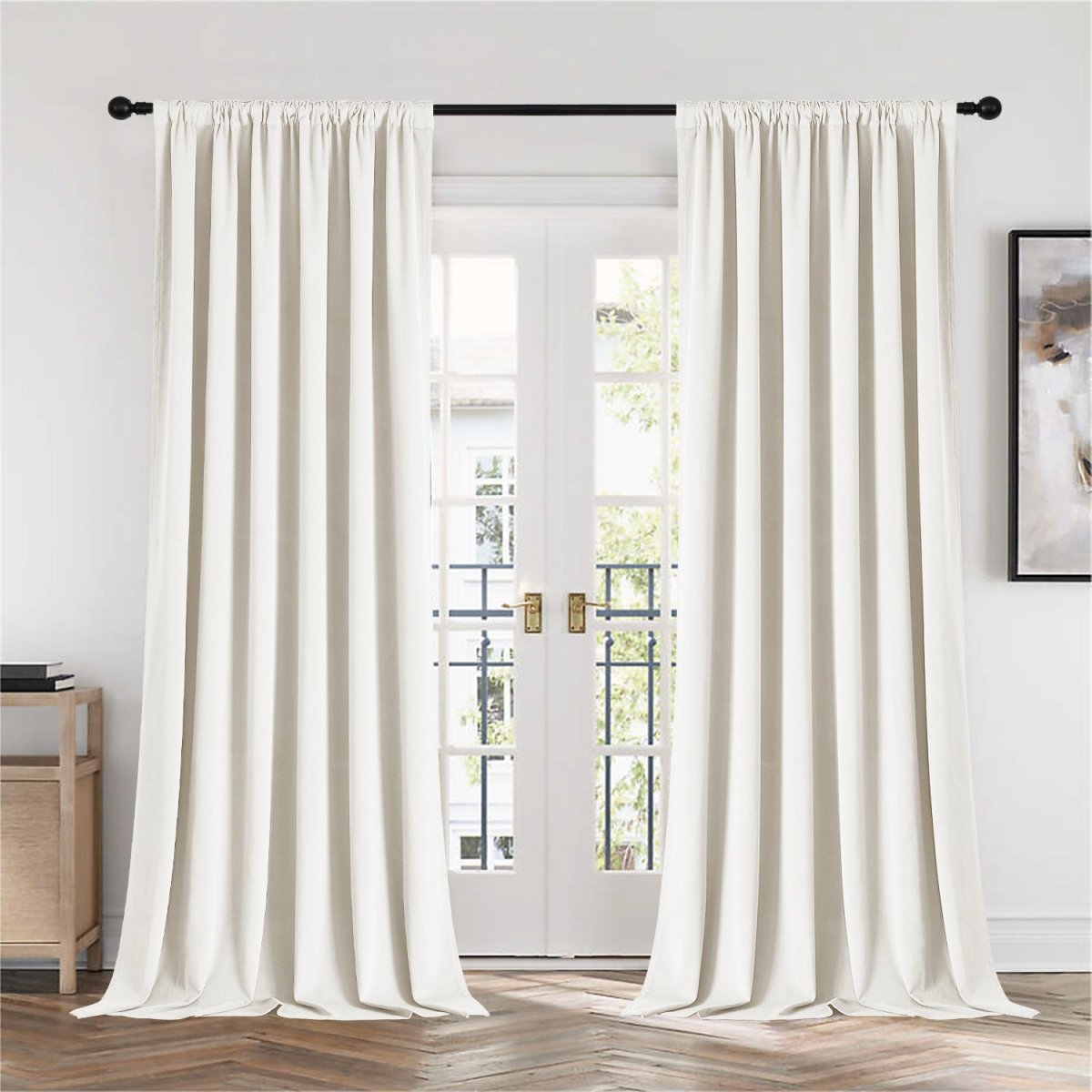 Two cream Joydeco velvet blackout curtains on black rod, French doors, wooden cabinet, and abstract art in room.