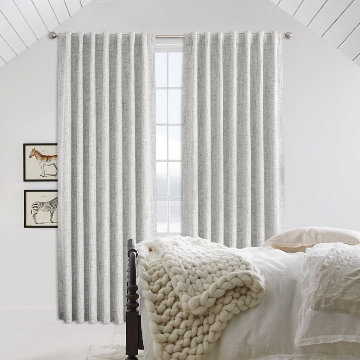 Light gray linen blackout curtains with back tab rod pocket hanging from silver rod in a bedroom.