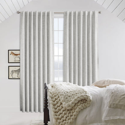 Light gray linen blackout curtains with back tab rod pocket hanging from silver rod in a bedroom.