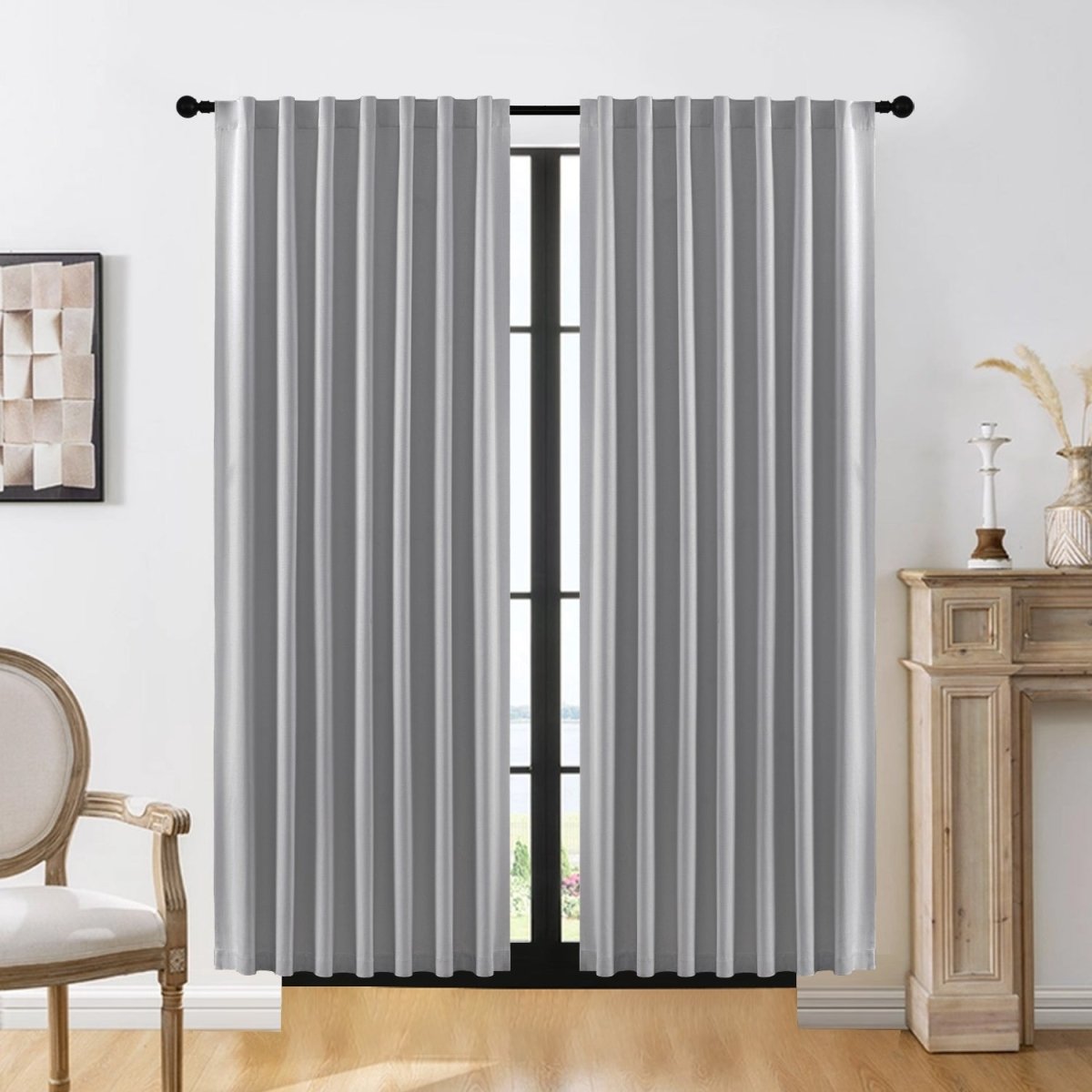Two light gray Joydeco blackout curtains with vertical pleats on a black rod in a living room.