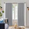 Two light gray Joydeco blackout curtains with soft vertical pleats hanging from a black rod in a living room.