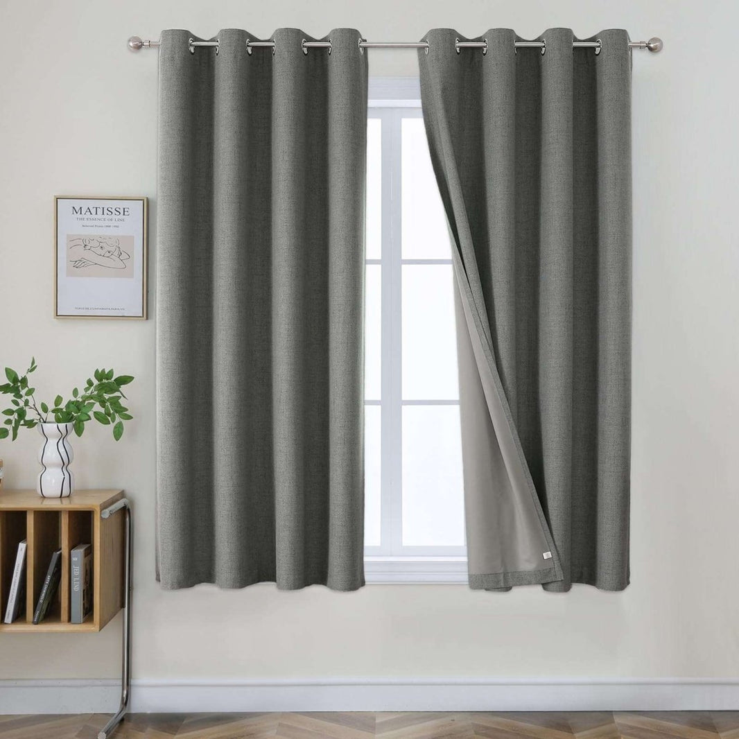 Two grey linen blackout curtains with grommets, one panel partially open revealing a lighter lining.