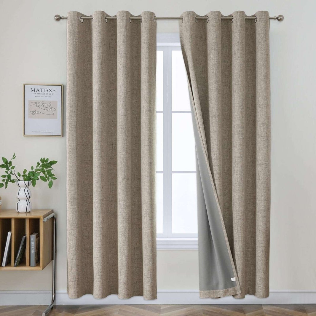Two beige faux linen blackout curtains with grommet tops hanging on a rod, one panel slightly open to show grey liner.