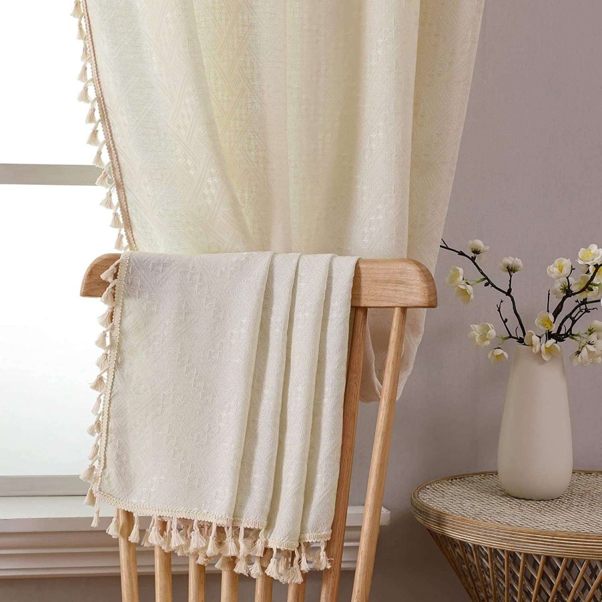 Creamy beige Joydeco boho linen curtains with geometric embroidery and tassels draped on a wooden chair, showcasing texture.