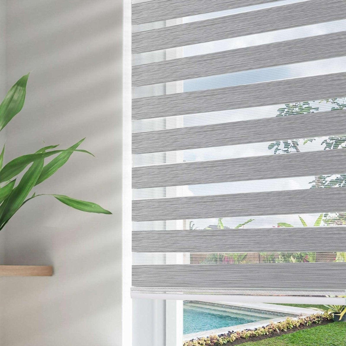 Grey blackout zebra shades with dual light filtering layers, showing view of pool and garden through window.
