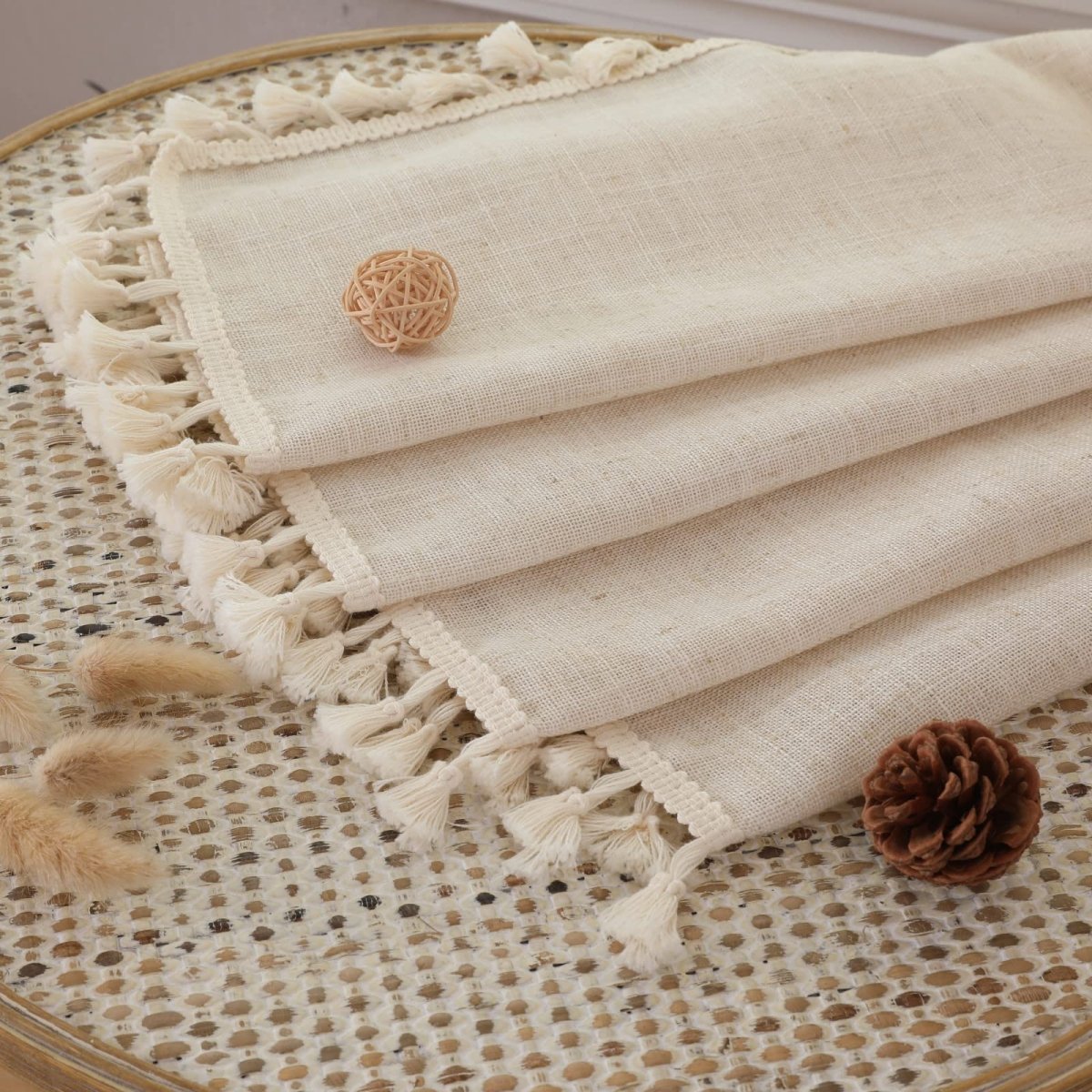 Close-up of cream linen curtains with crochet trim and tassels, showing fabric texture detail.