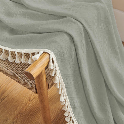 Close-up of boho grayish-green linen sheer curtain with geometric pattern and cream tassels, draped on wicker chair.
