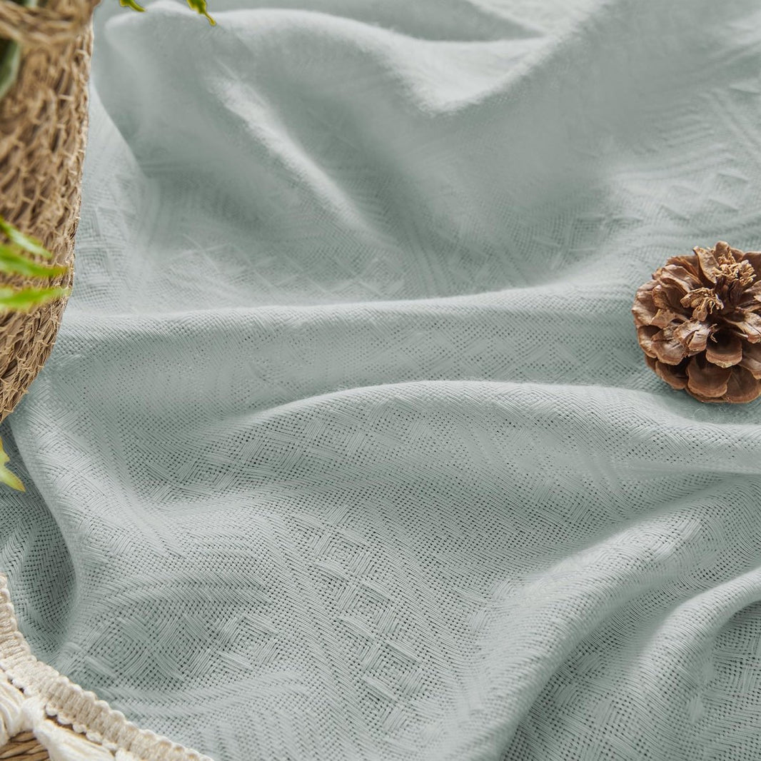 Close-up of ice blue linen sheer curtain with cream tassels and a pinecone, highlighting boho farmhouse texture.