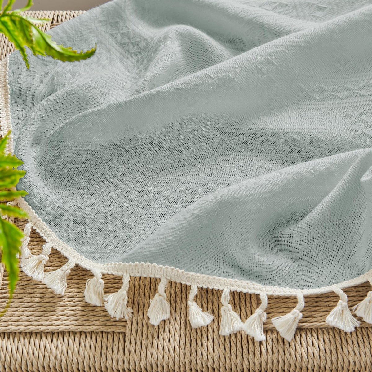 Close-up of ice blue linen fabric with subtle geometric pattern and cream tassels, showcasing boho farmhouse texture.