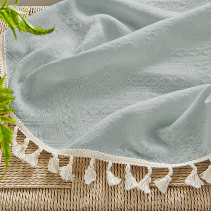 Close-up of ice blue linen fabric with subtle geometric pattern and cream tassels, showcasing boho farmhouse texture.