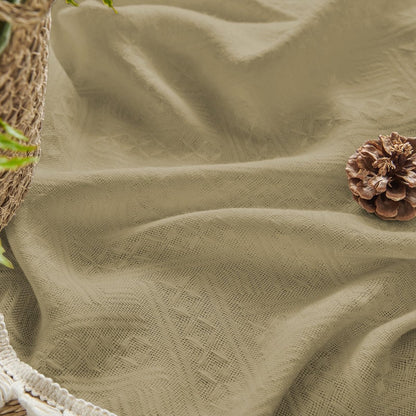 Close-up of khaki linen fabric with diamond pattern, cream tassel trim, and pinecone. Boho farmhouse curtain texture.