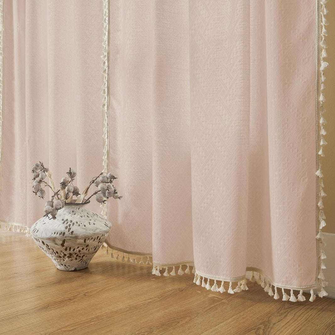 Close up of light pink boho linen sheer curtains with tassel fringe and cream ribbon trim on living room floor.