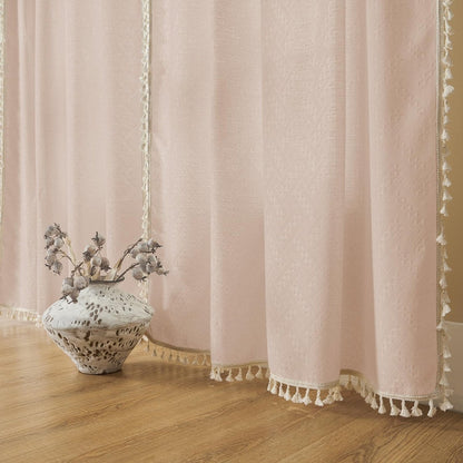 Close up of light pink boho linen sheer curtains with tassel fringe and cream ribbon trim on living room floor.