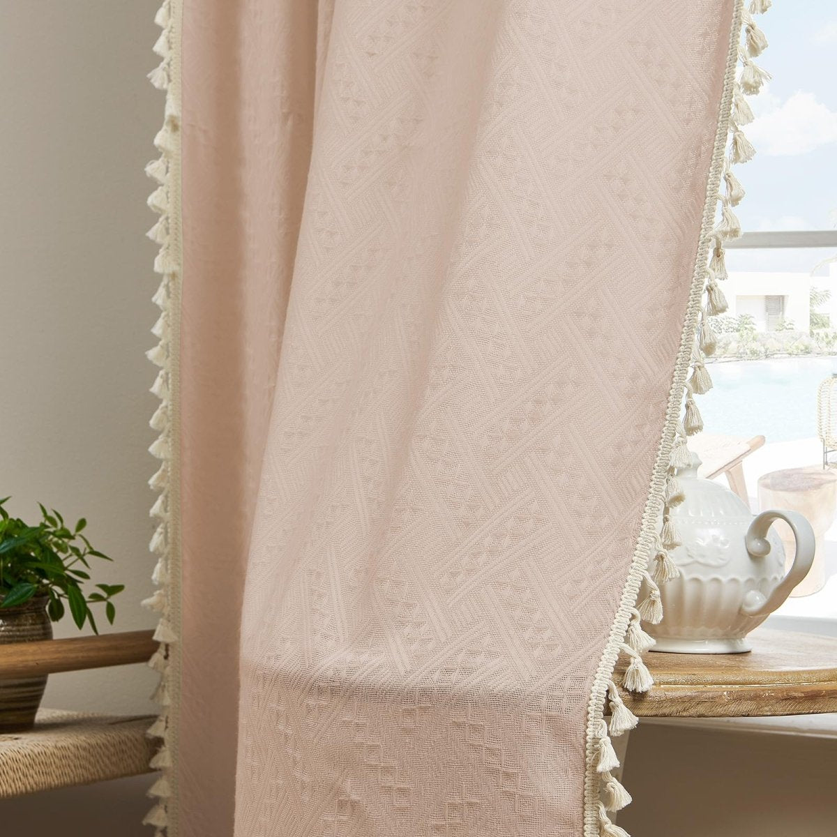 Close-up of light pink boho linen sheer curtain with geometric pattern, tassel fringe, and ribbon trim.