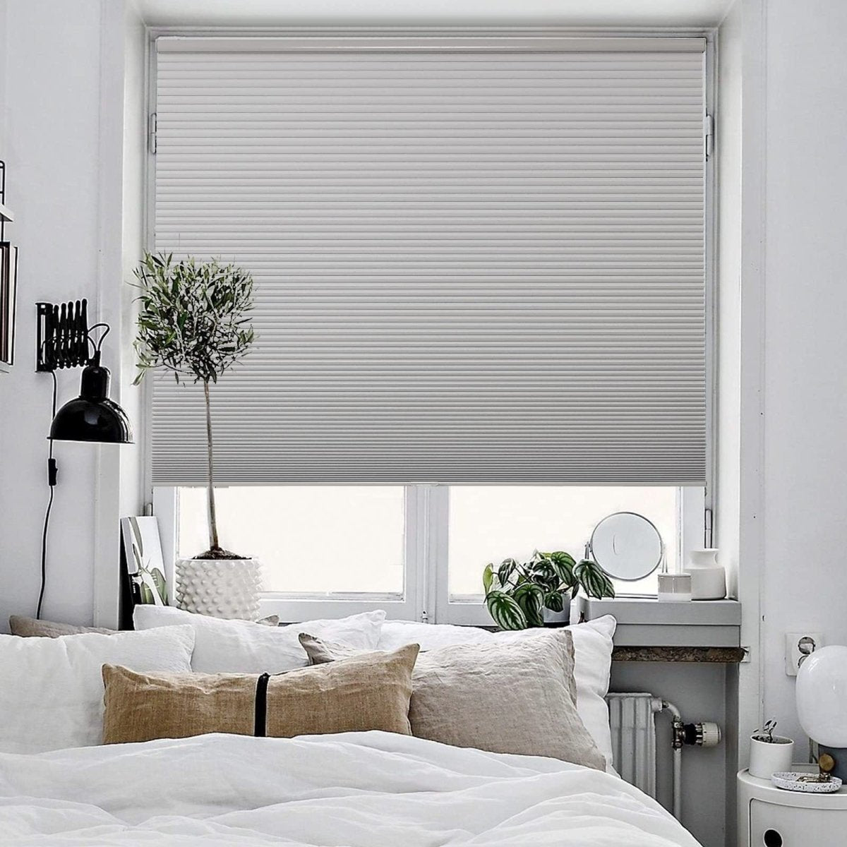 Light grey cordless blackout cellular shade on a window above a bed, showing pleated honeycomb design in a modern bedroom.