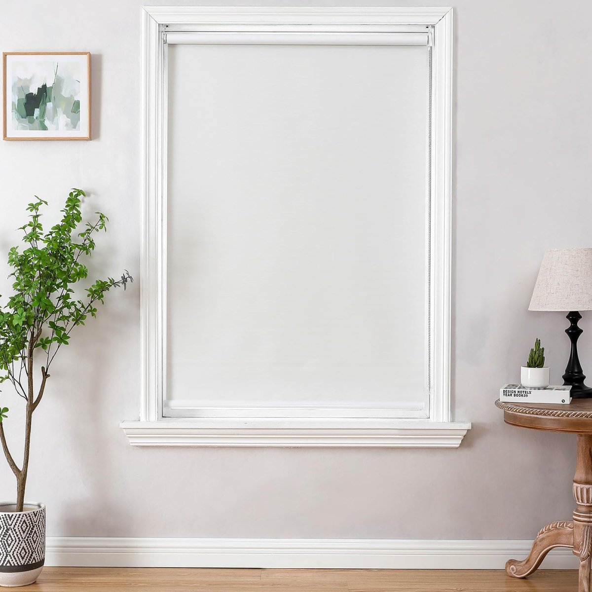 White blackout roller shade with metal chain installed in a bright room with gray walls and plant.