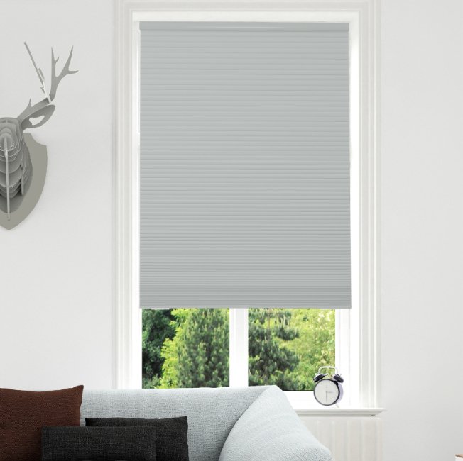 Joydeco light grey cordless blackout cellular shade installed in a white window with a view of trees.