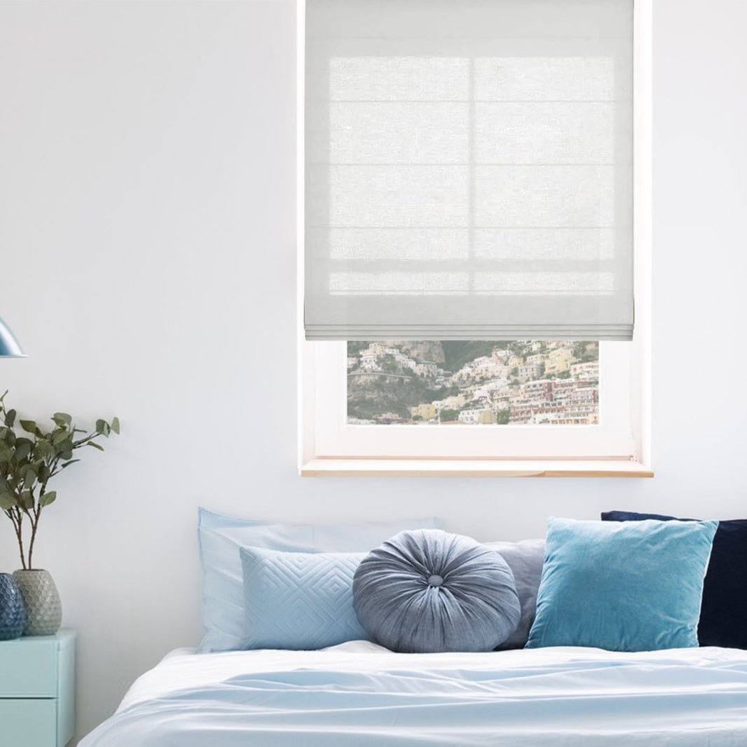 Joydeco off-white linen blend Roman shade with horizontal pleats filters light in a bedroom.