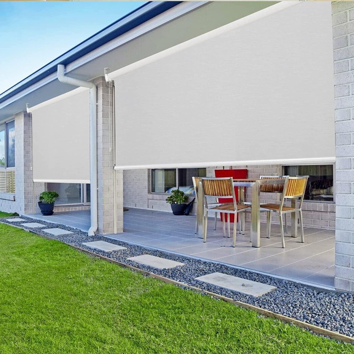 Two white Joydeco 100% blackout roller shades installed on a modern patio with outdoor furniture visible.