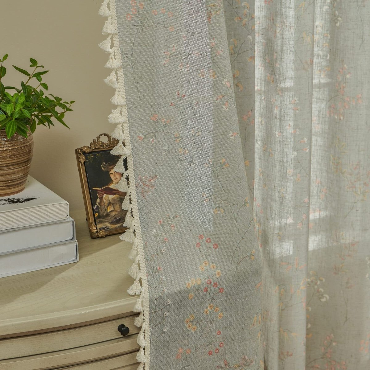 Light blue sheer linen curtains with scattered floral embroidery and white tassel trim detail.