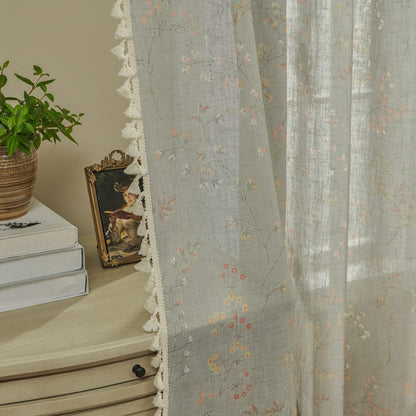 Light blue sheer linen curtains with scattered floral embroidery and white tassel trim detail.