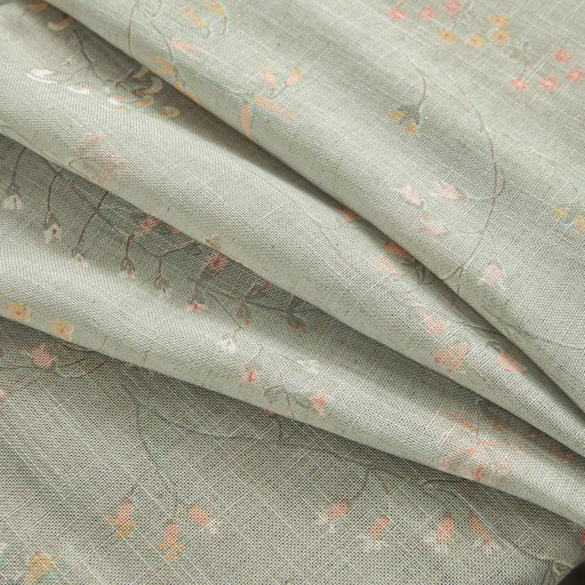 Close-up of beige linen sheer curtain fabric with small pink and yellow floral pattern, showing texture.