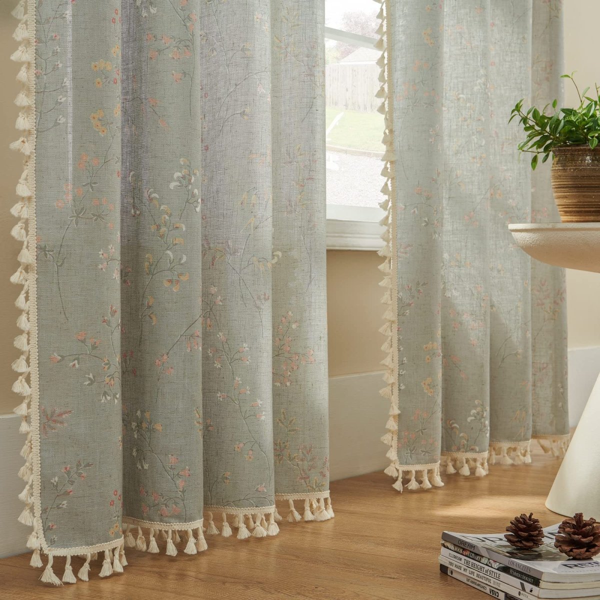 Light blue linen sheer curtains with scattered floral pattern and cream tassel trim detail.