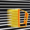 Joydeco handheld blinds cleaner with orange handle and yellow brush cleaning black and white horizontal blinds slats.