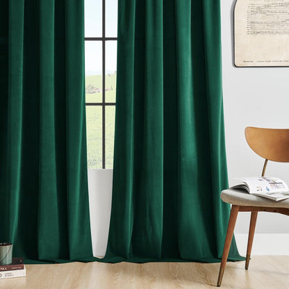 Joydeco luxury green velvet blackout curtains, plush fabric texture, framing a sunlit window. Elegant home decor.