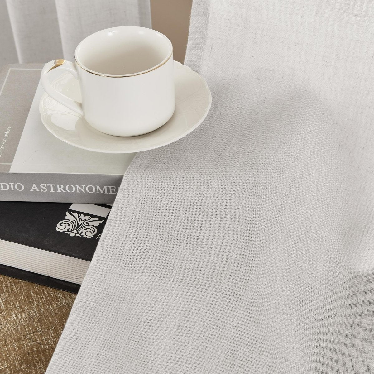 Joydeco Blanc De Blanc white linen curtains, close-up of natural weave texture with teacup and books.