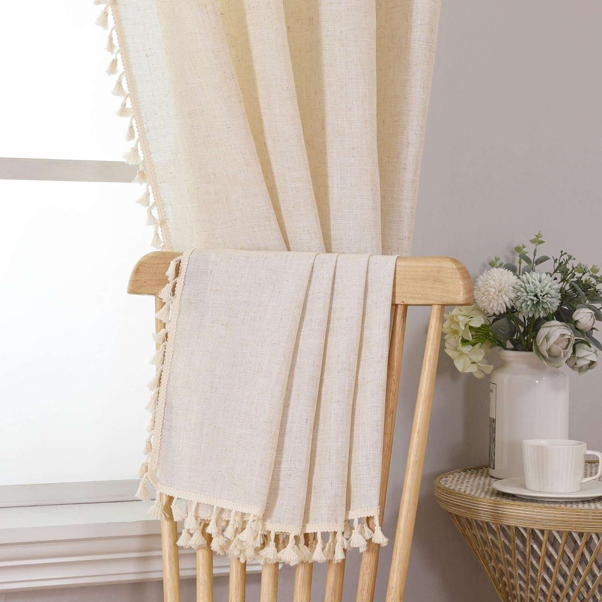 Joydeco solid beige boho curtains with tassel trim and embroidery, natural linen texture, shown draped on a chair.
