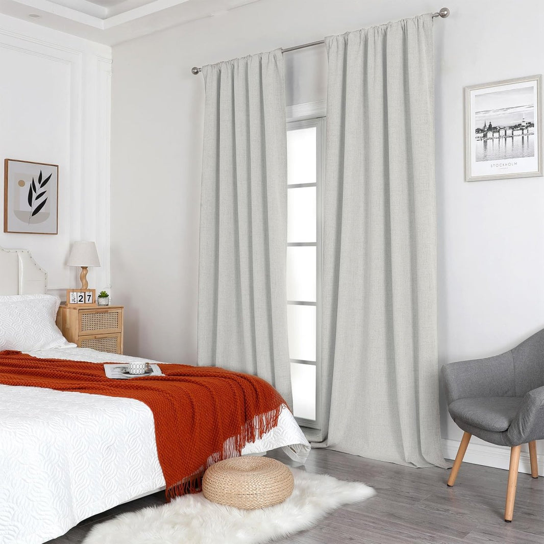 Joydeco white linen blackout curtains hung on silver rod in a bedroom setting with a bed and armchair.